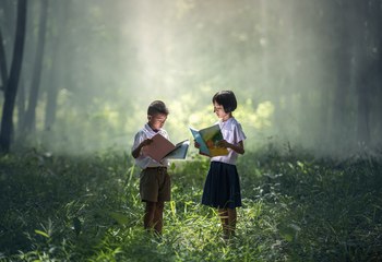 due ragazzini guardano un quaderno immersi in una foresta